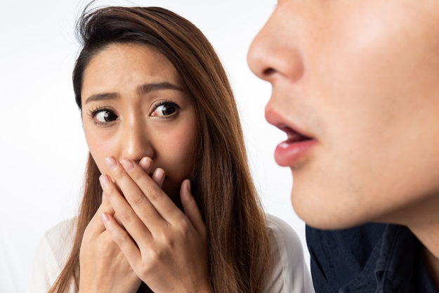 causes of bad breath (1) woman covering her face so as not to smell the bad breath of the woman speaking next to her