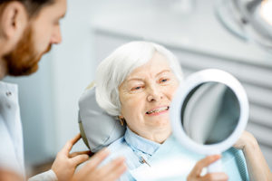 woman looking at her new dentures in a mirror