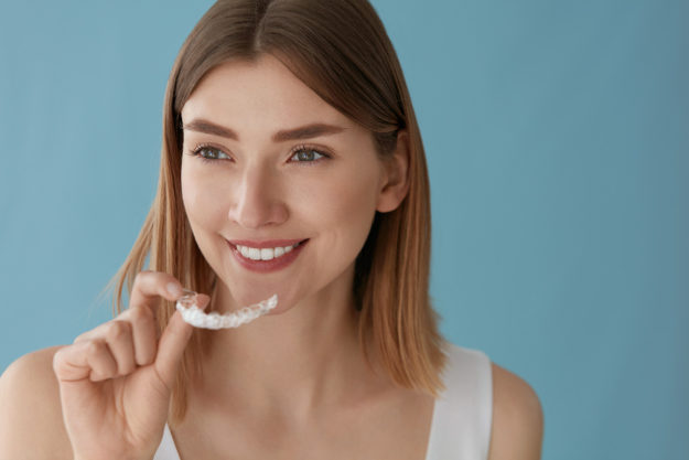 how to prevent teeth shifting (1) smiling woman putting her retainer in to prevent teeth shifting